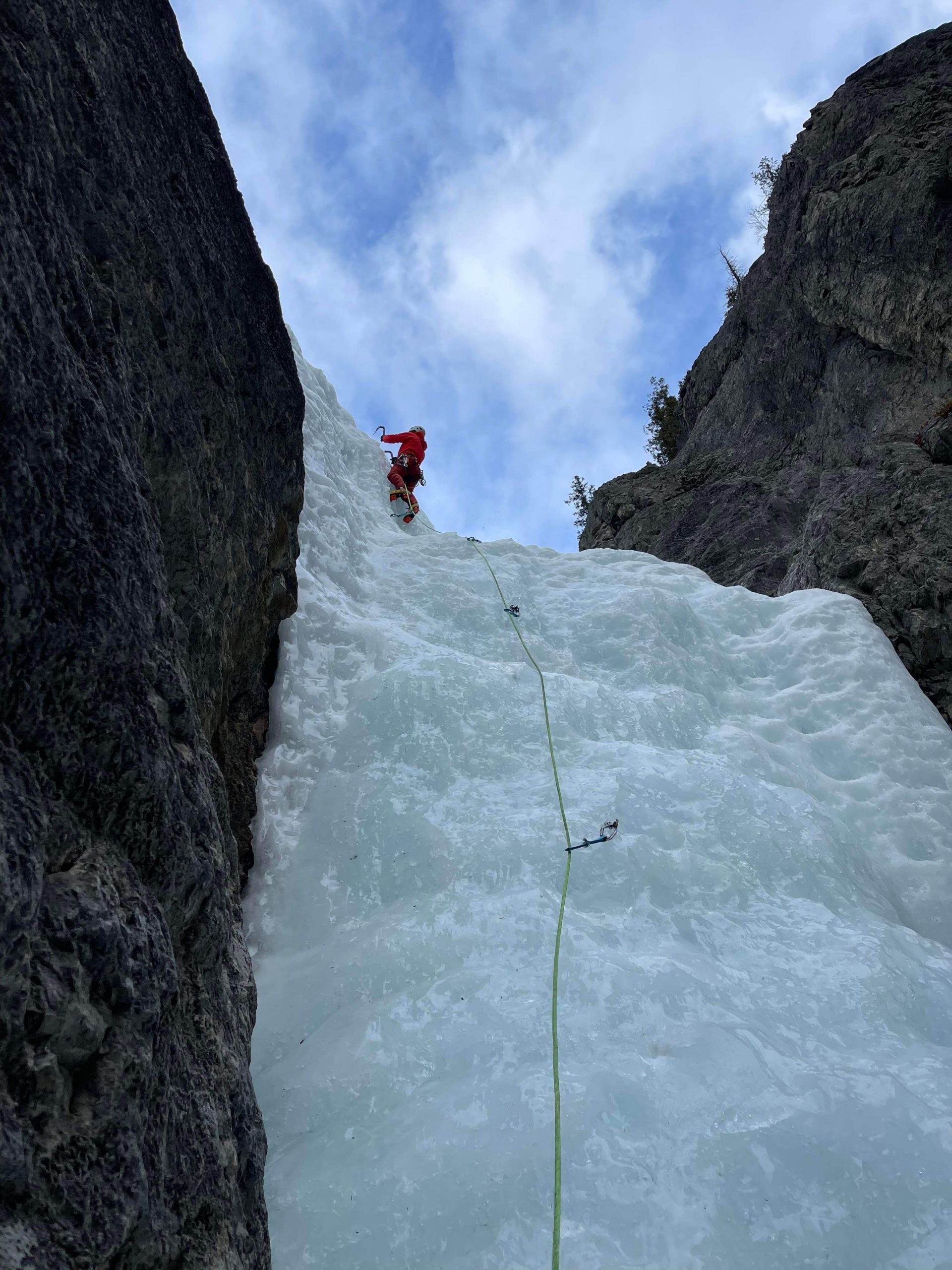 An ice climber leading a frozen waterfall between limestone walls